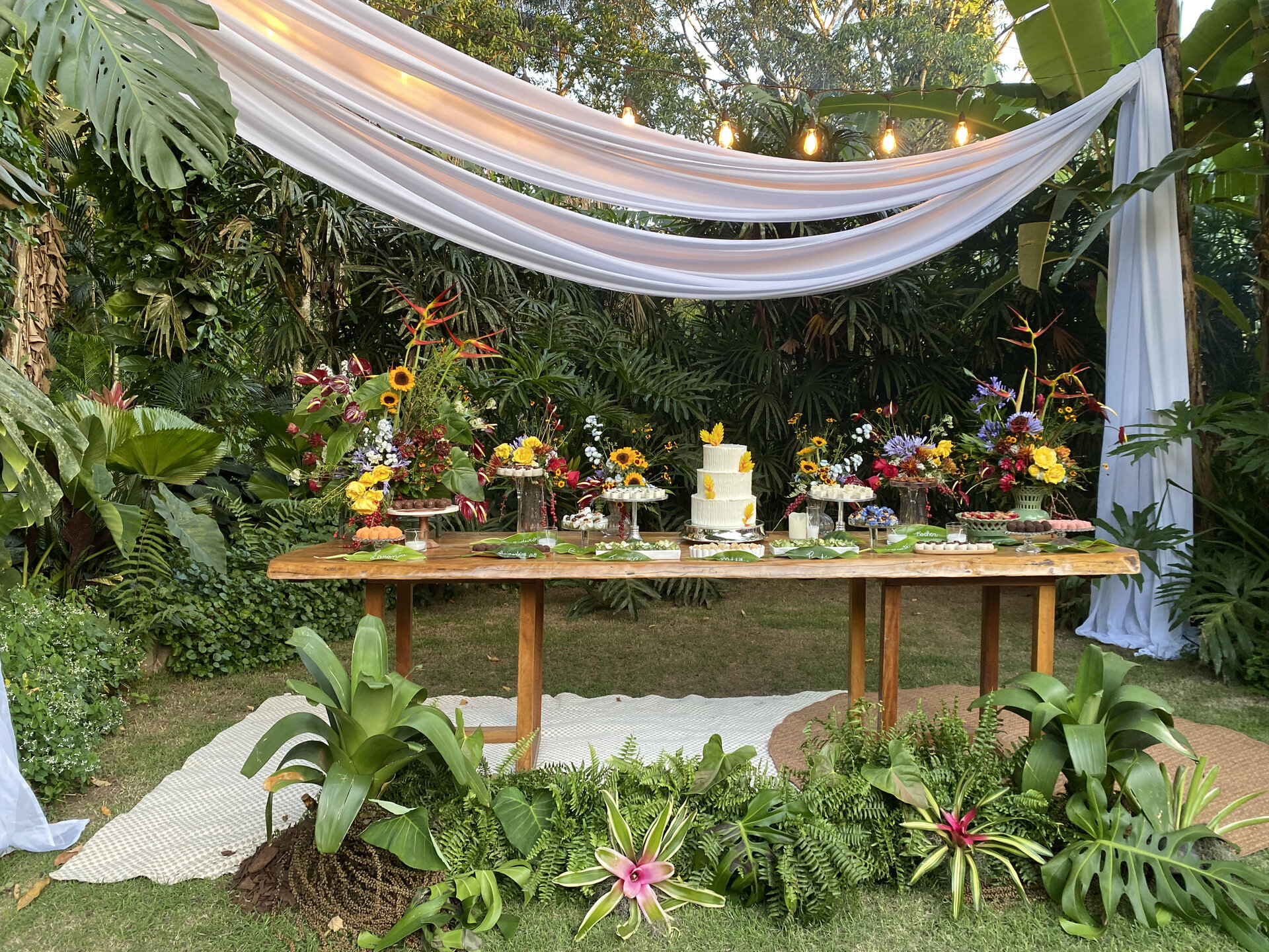 Mesa de doces decorada sob drapeados no jardim do Jamboo